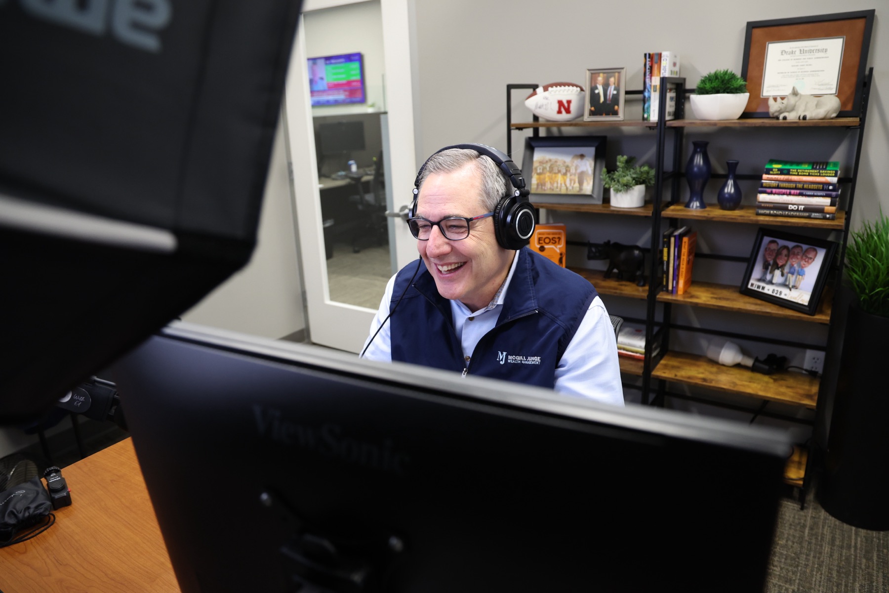 Ed McGill laughing in headphones behind the monitor in the LED podcast studio
